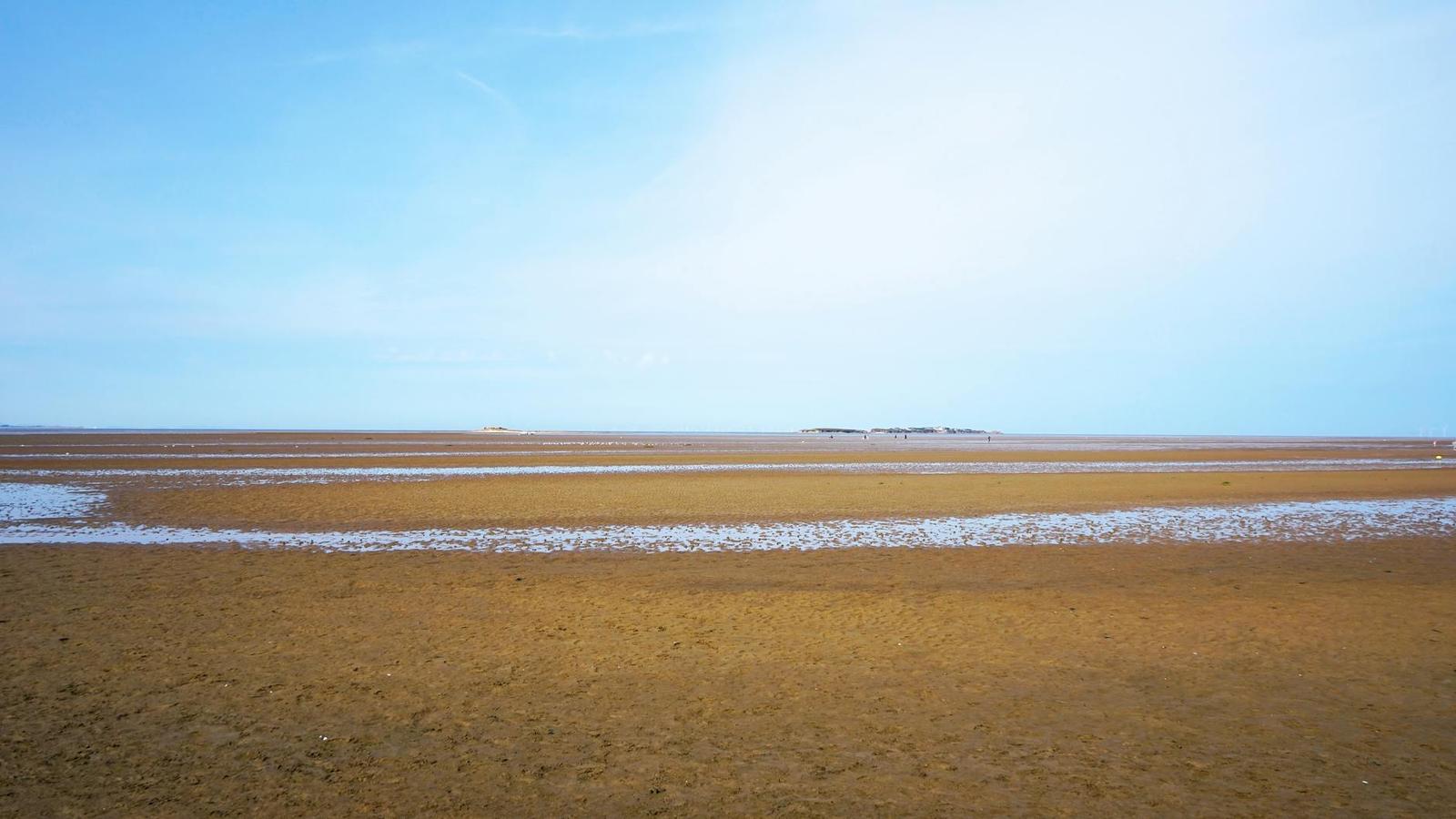 A wide flat tidal beach under a pale blue sky
