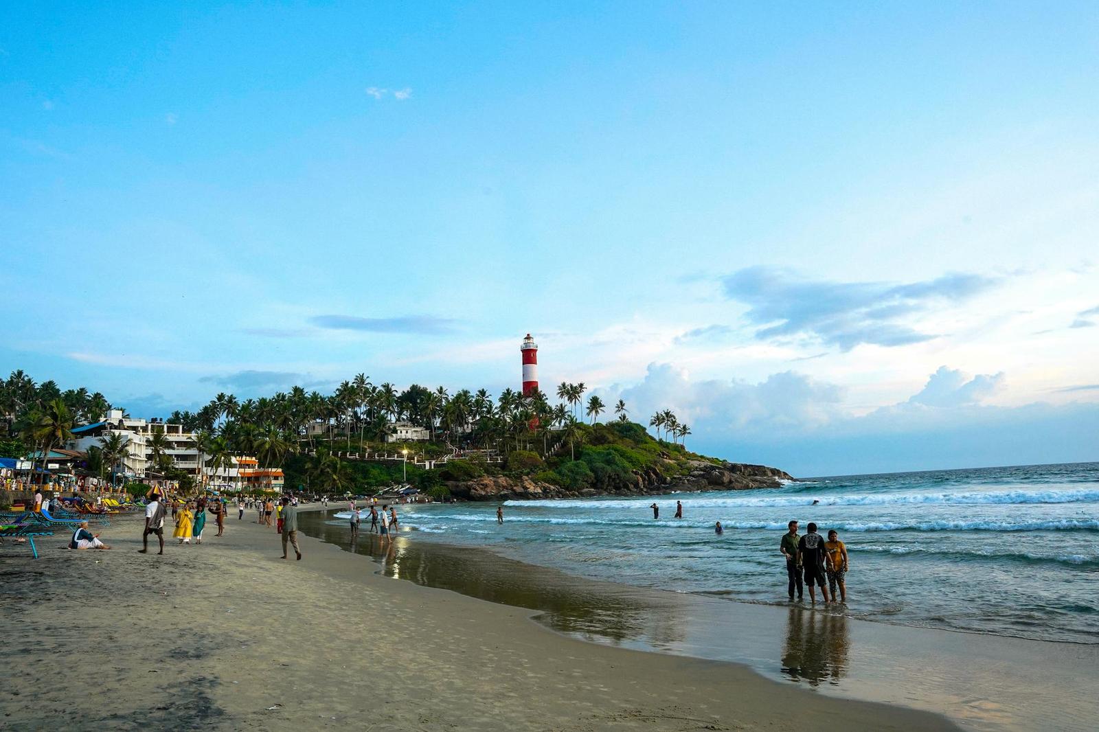 People wading at a beach shoreline with a striped lighthouse on the point
