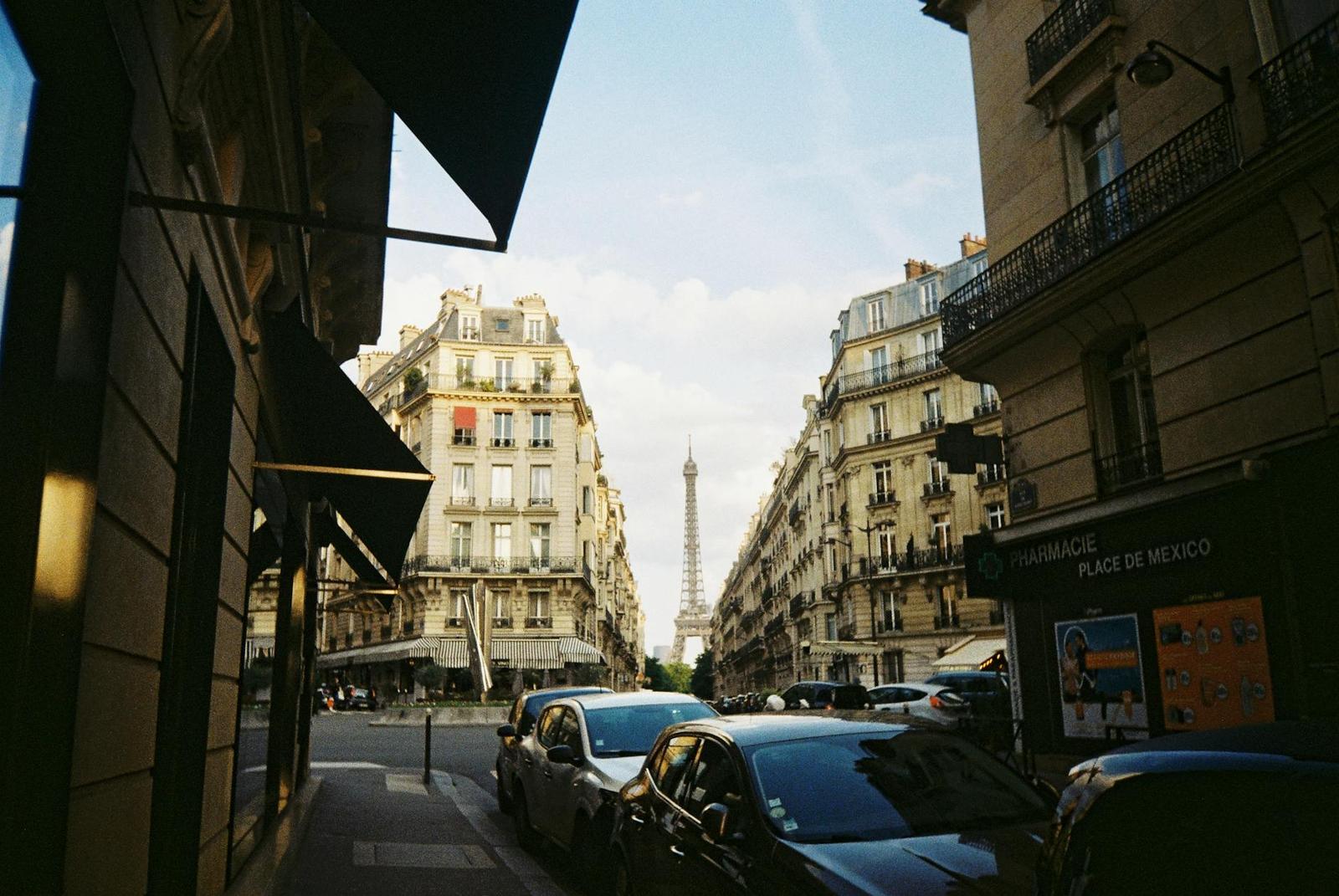 A classic Paris cityscape featuring the Eiffel Tower framed by elegant Haussmann buildings in a busy street