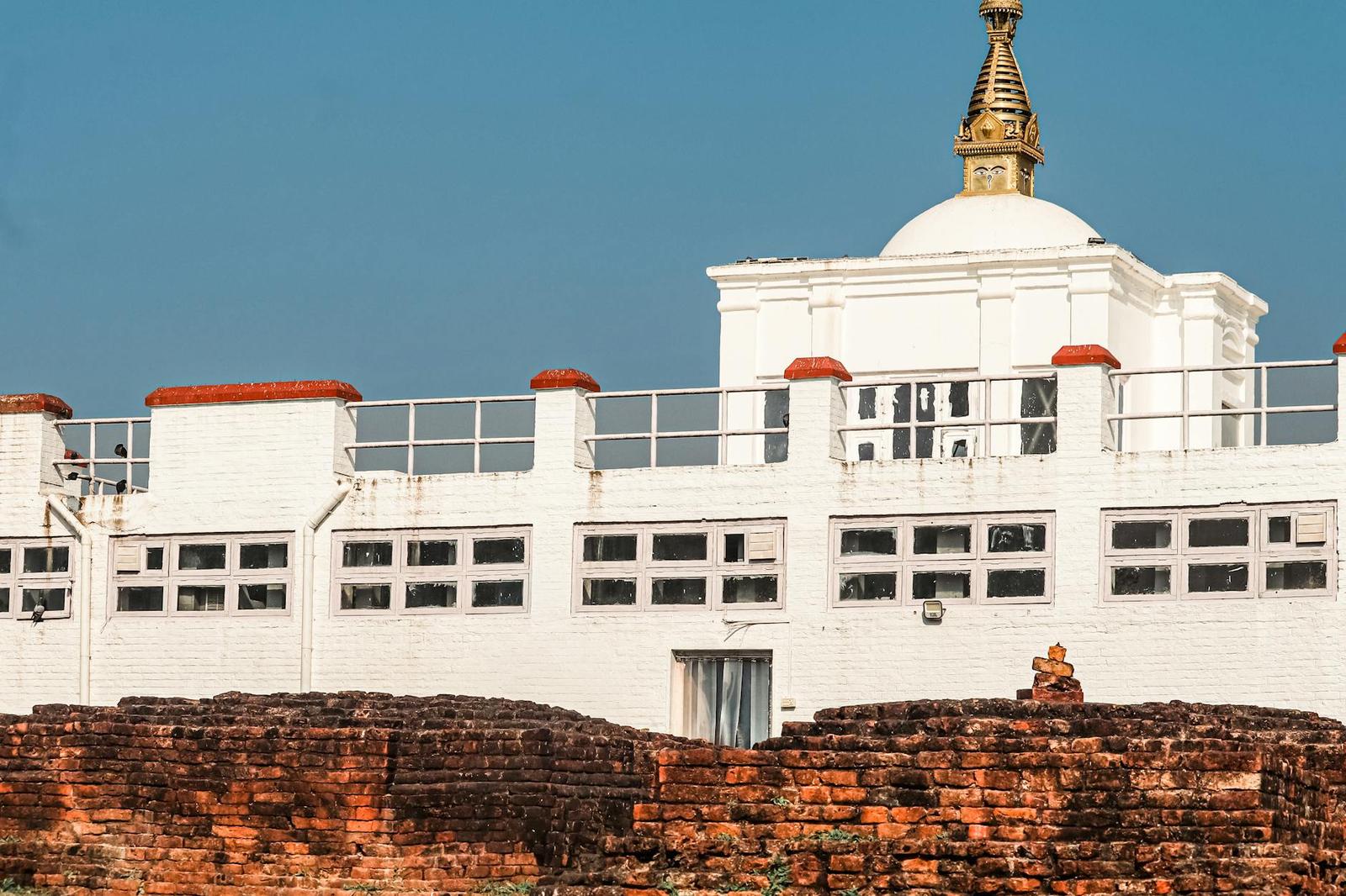 A whitewashed stupa building with a golden spire behind a low brick wall