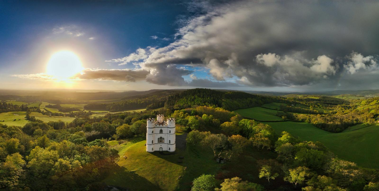 A turreted stone manor rising from forest beneath a golden sunset