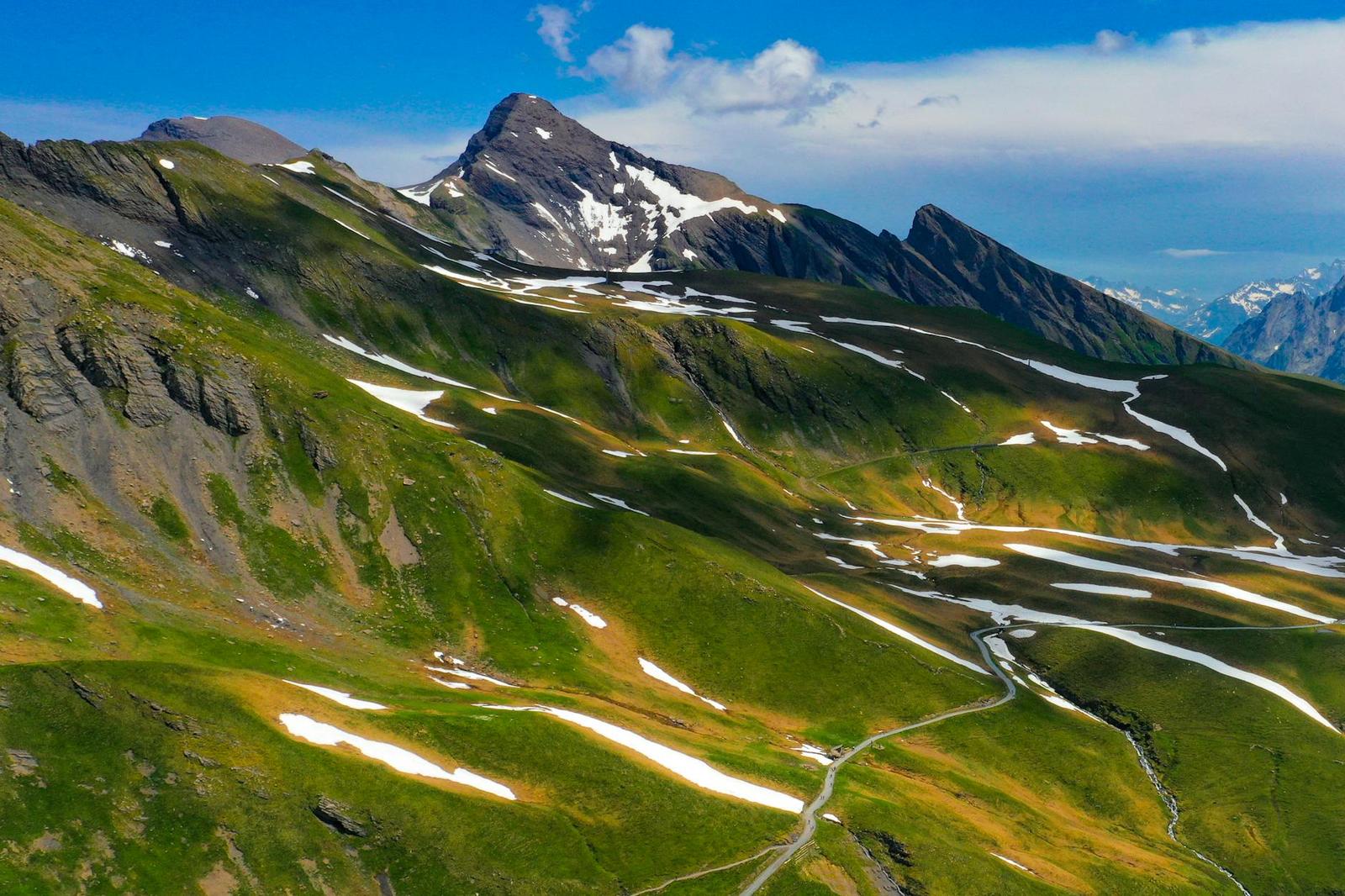 Aerial view of a green mountain ridge streaked with patches of snow