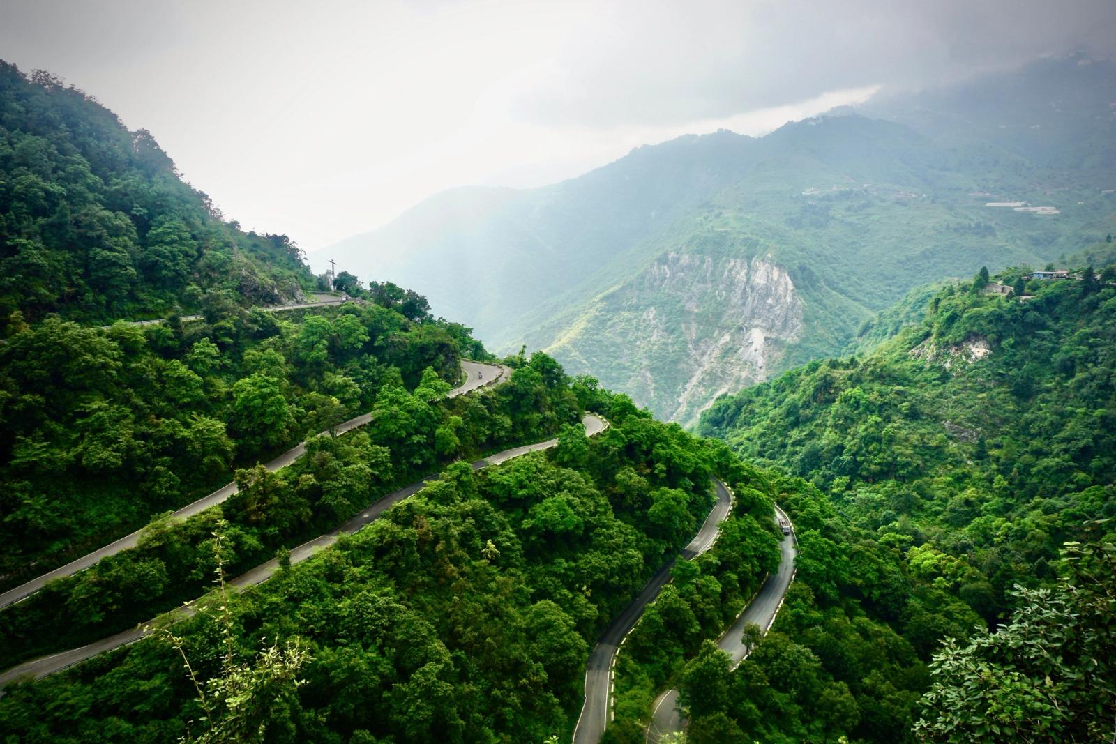Aerial shot of lush green mountains with winding roads under cloudy skies
