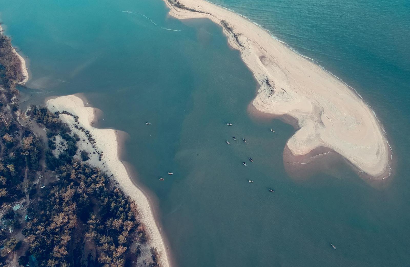 Aerial view of a sandbar reaching into turquoise water with small boats