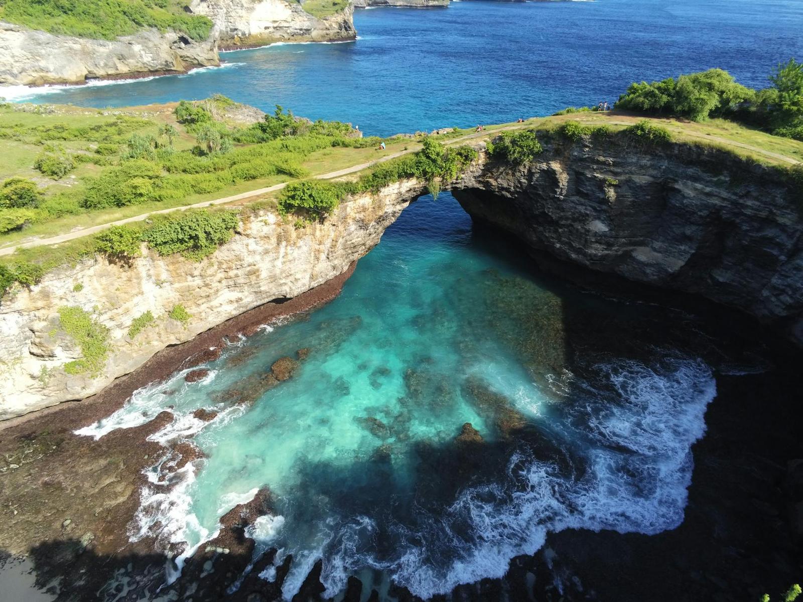 Aerial view of a natural rock arch over a turquoise lagoon on a cliff coastline