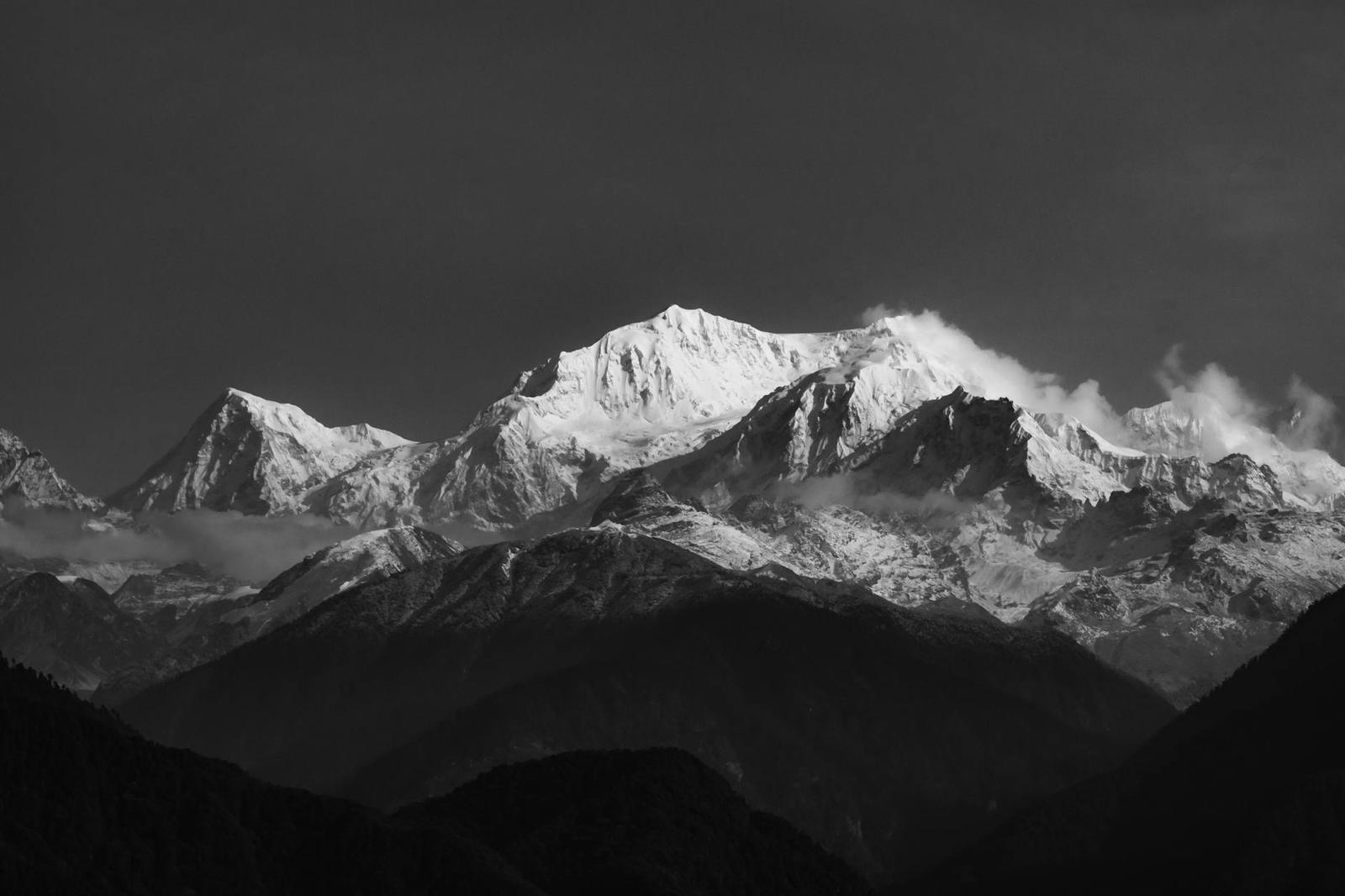A black and white view of snow capped peaks under dramatic light
