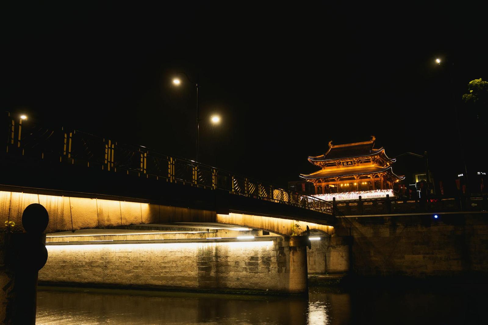 An illuminated lantern-lit pavilion beside a stone bridge at night