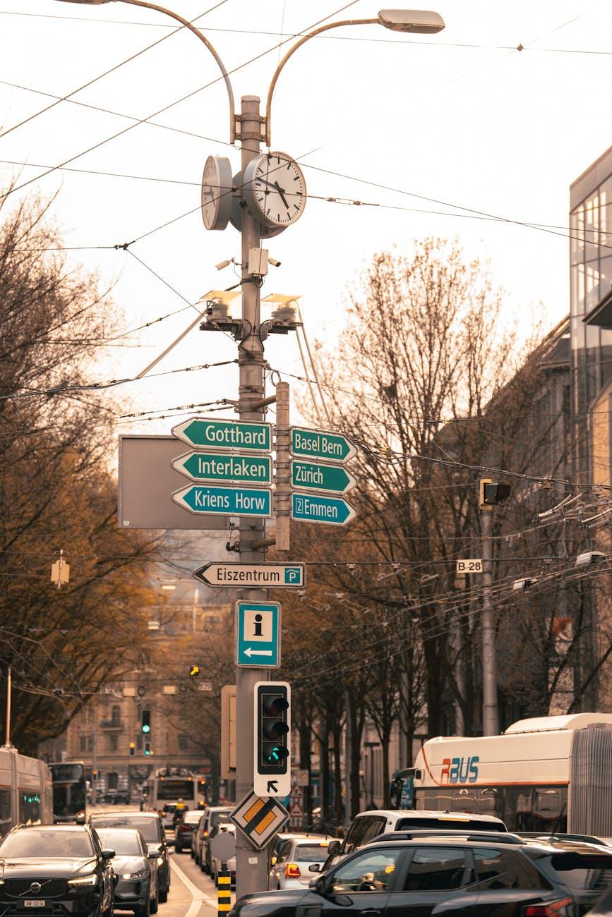 City clock and directional signs mounted over a busy intersection
