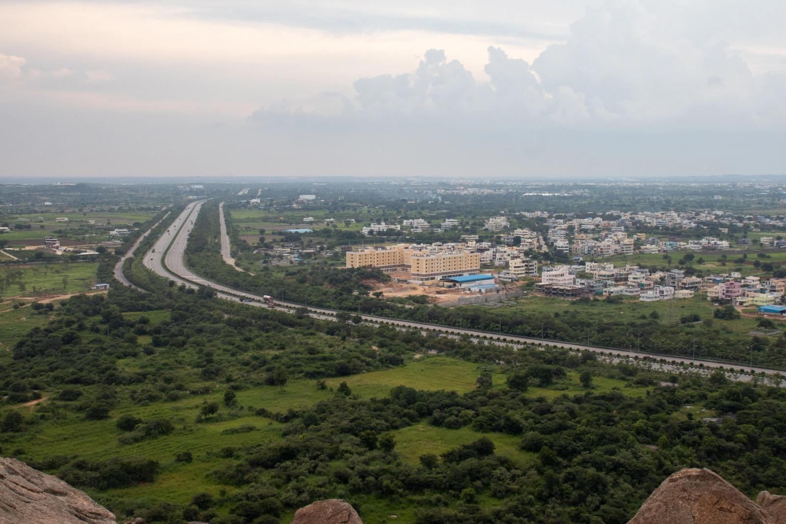 Aerial view of a lush green Indian landscape with a highway stretching through fields and residential areas