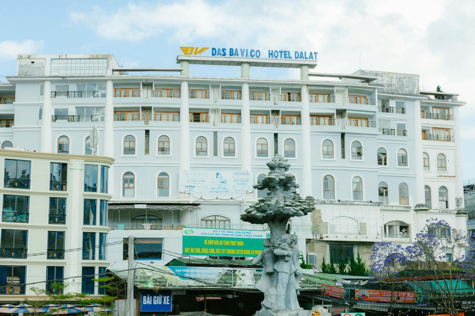 White multi-storey hotel building with balconies behind a stone fountain statue