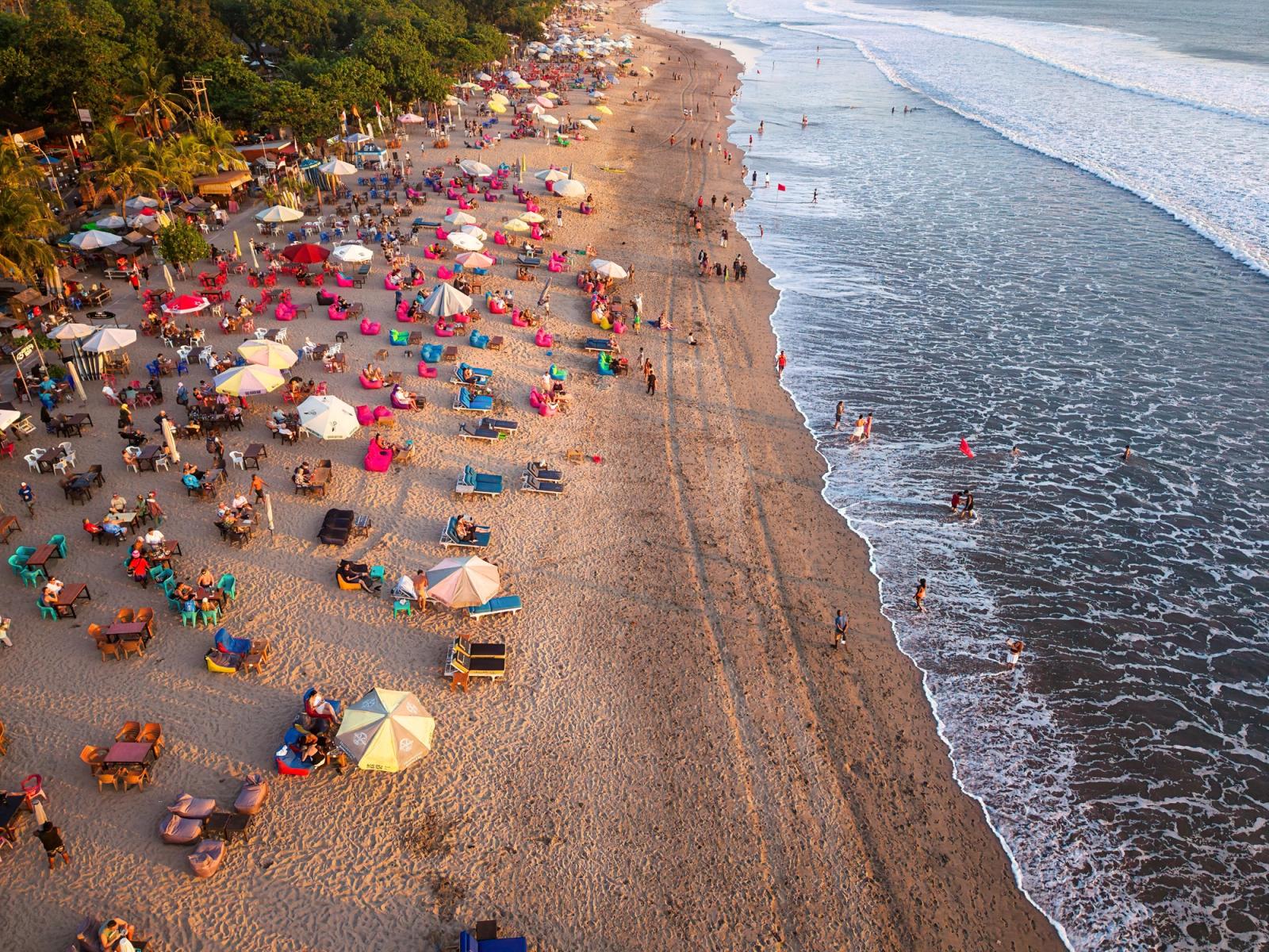 A lively beach scene in Bali, Indonesia, captured from above during sunset