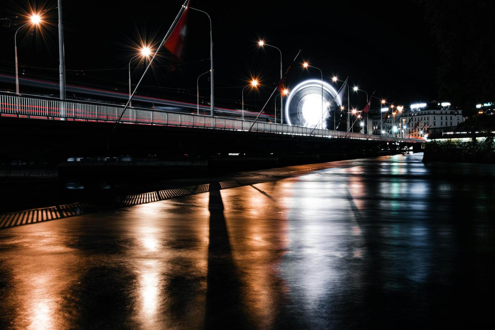 A wet riverside bridge glowing with streetlights and an illuminated ferris wheel at night