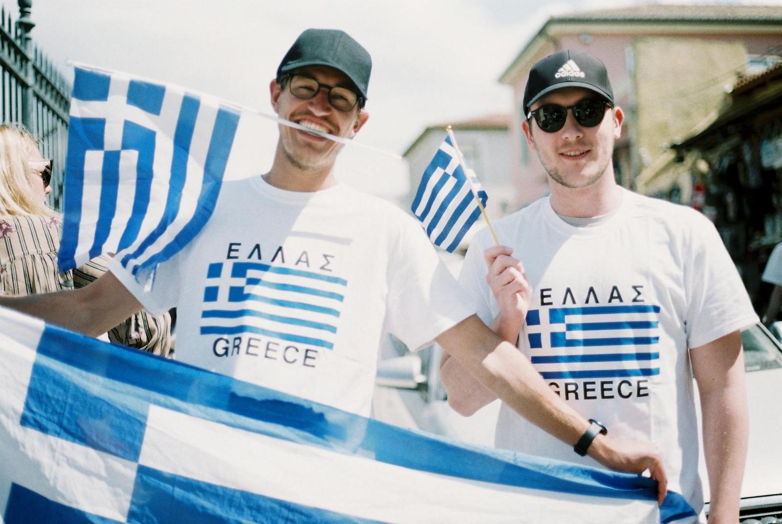 Two men in matching t-shirts holding national flags and smiling at the camera