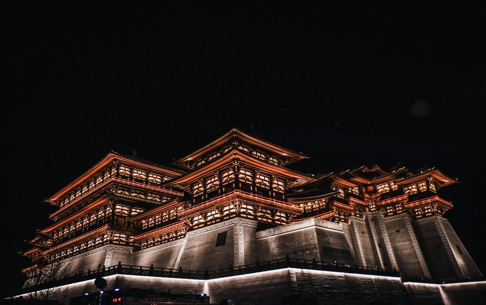 A multi-tiered pagoda temple illuminated in red and gold against a black night sky