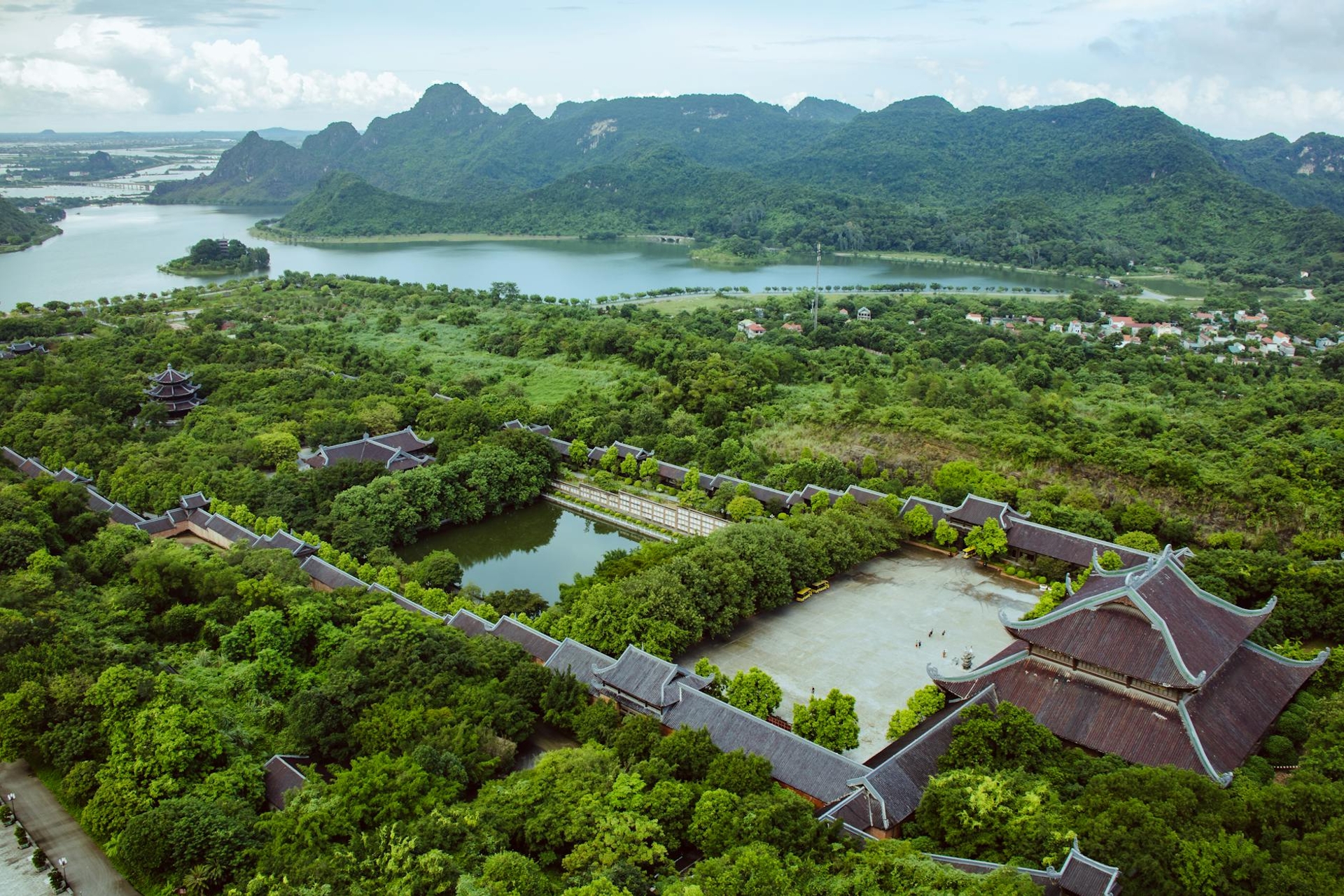 Aerial view of a temple complex with tiled roofs set among forested hills and a lake