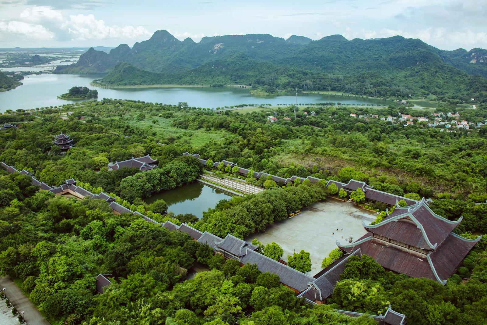 Aerial view of a temple complex with tiled roofs set among forested hills and a lake