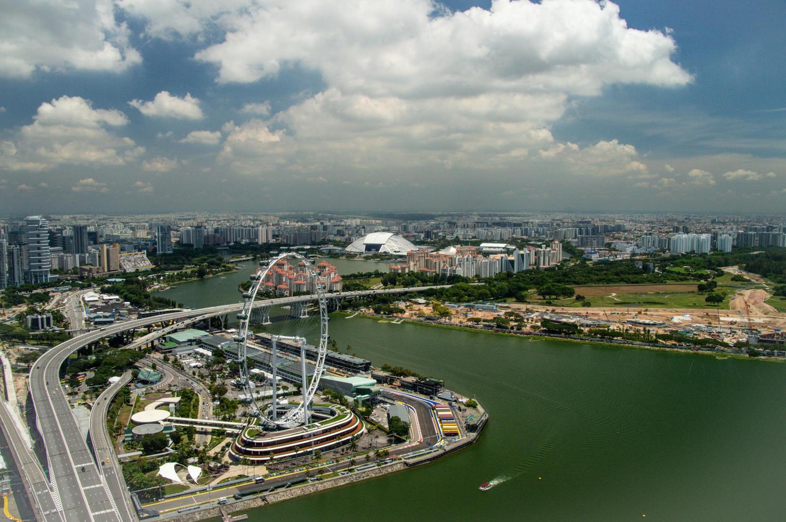 Aerial view of a riverside park with a giant observation wheel amid city towers