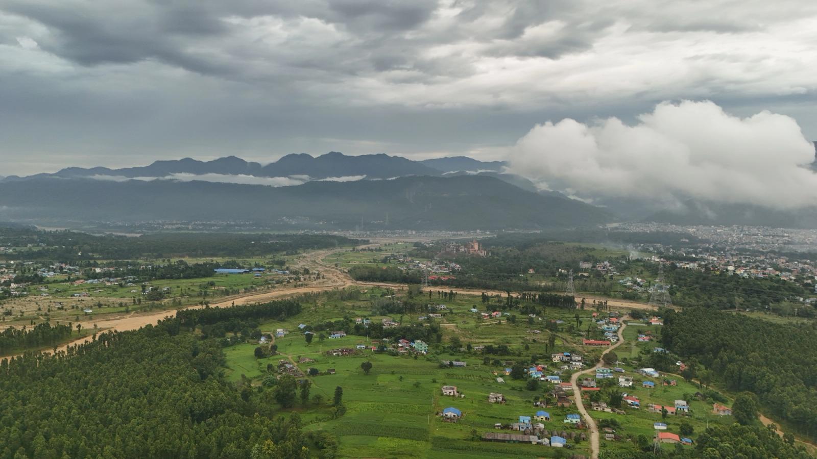 A breathtaking aerial view of a lush green valley and distant mountains under a cloudy sky in Nepal