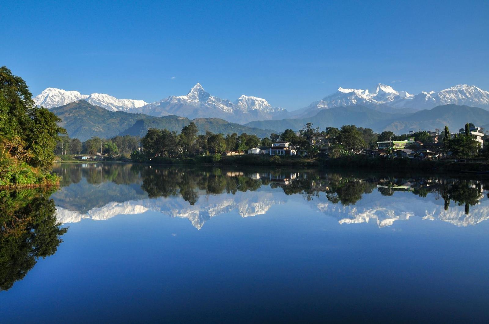 Snow-capped peaks mirrored in a still lake beside a lakeside town
