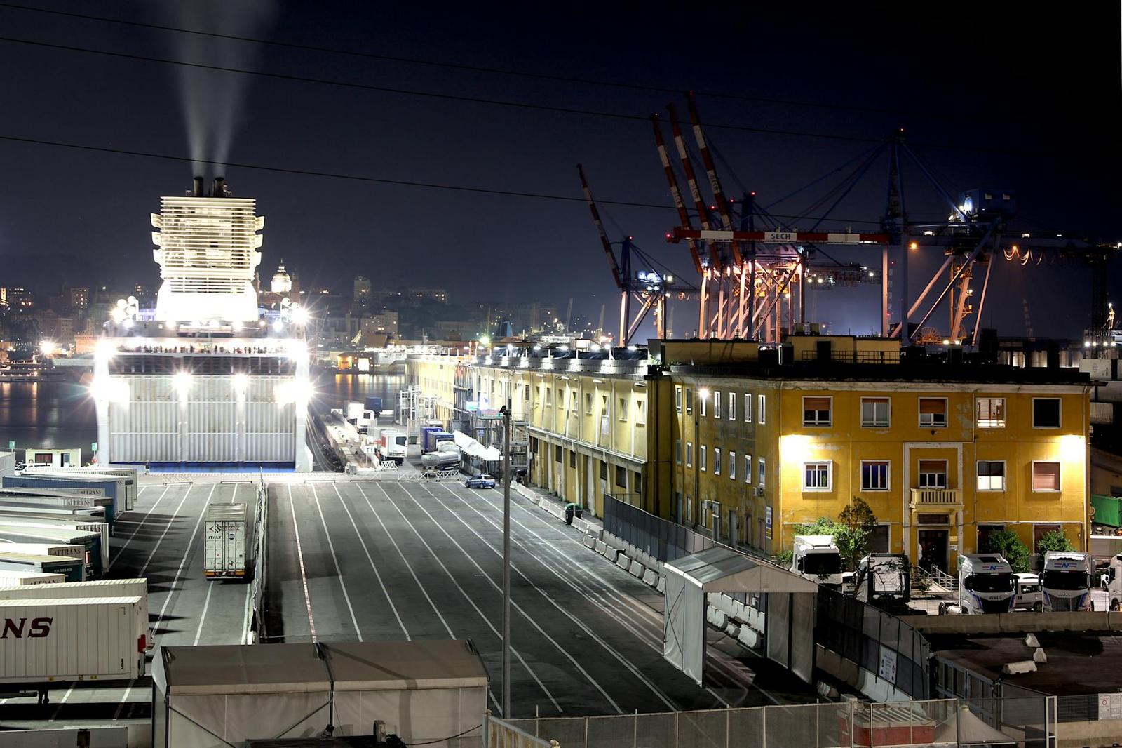 Night view of a shipping port with cranes and a ferry lit under floodlights