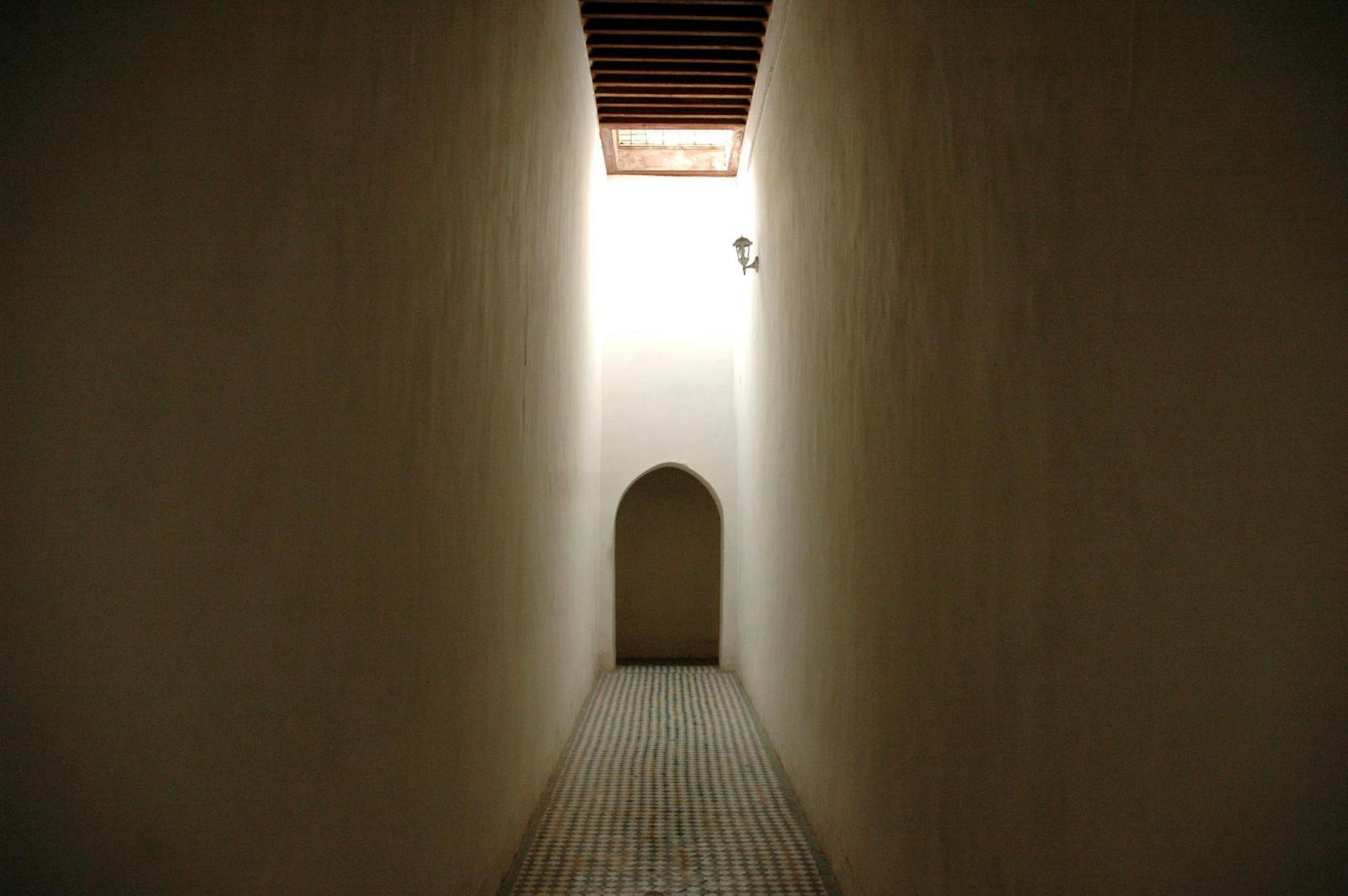 Narrow tiled corridor leading to an arched doorway lit from above