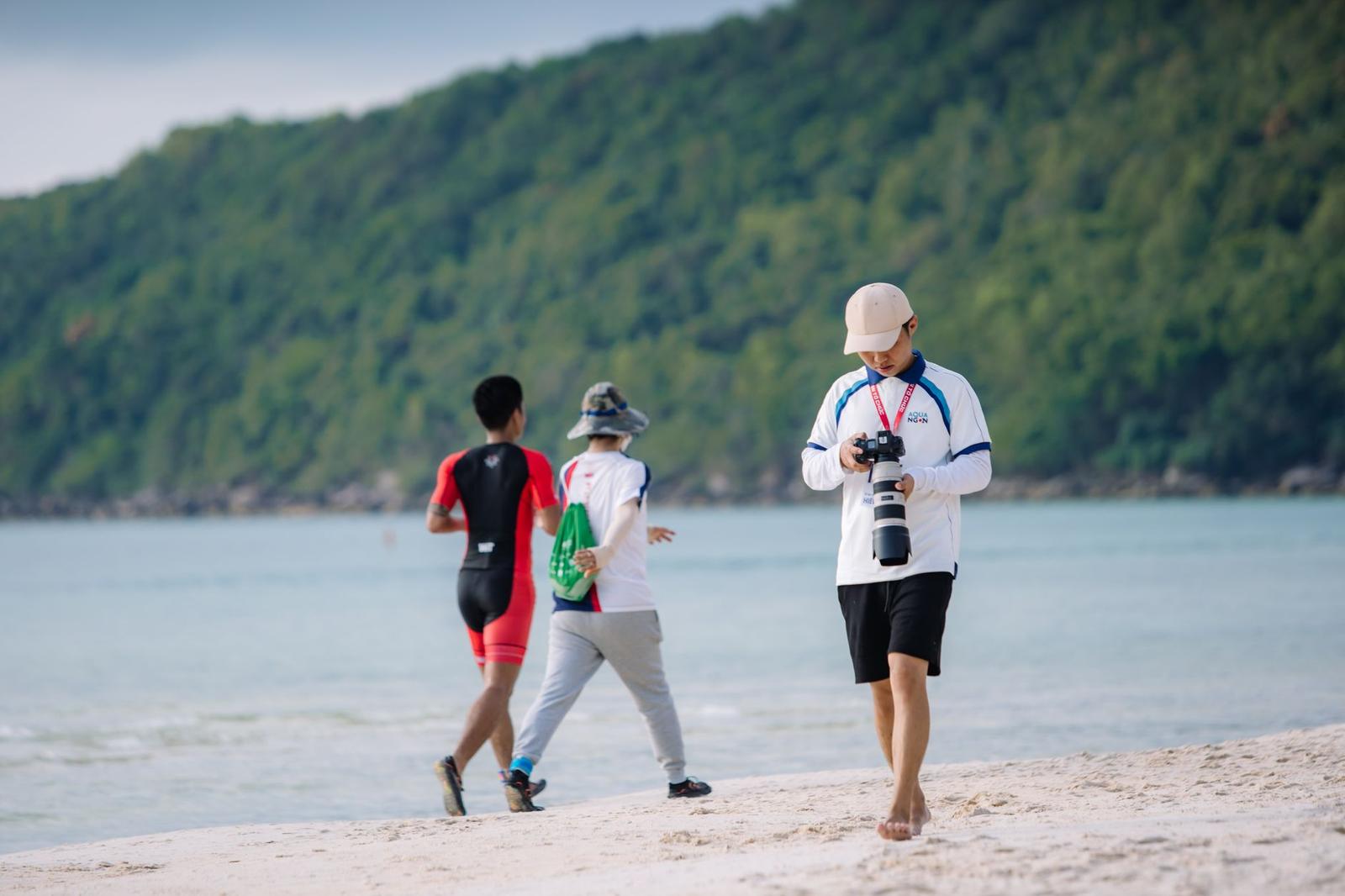 People walking along a sandy beach with a forested hillside behind