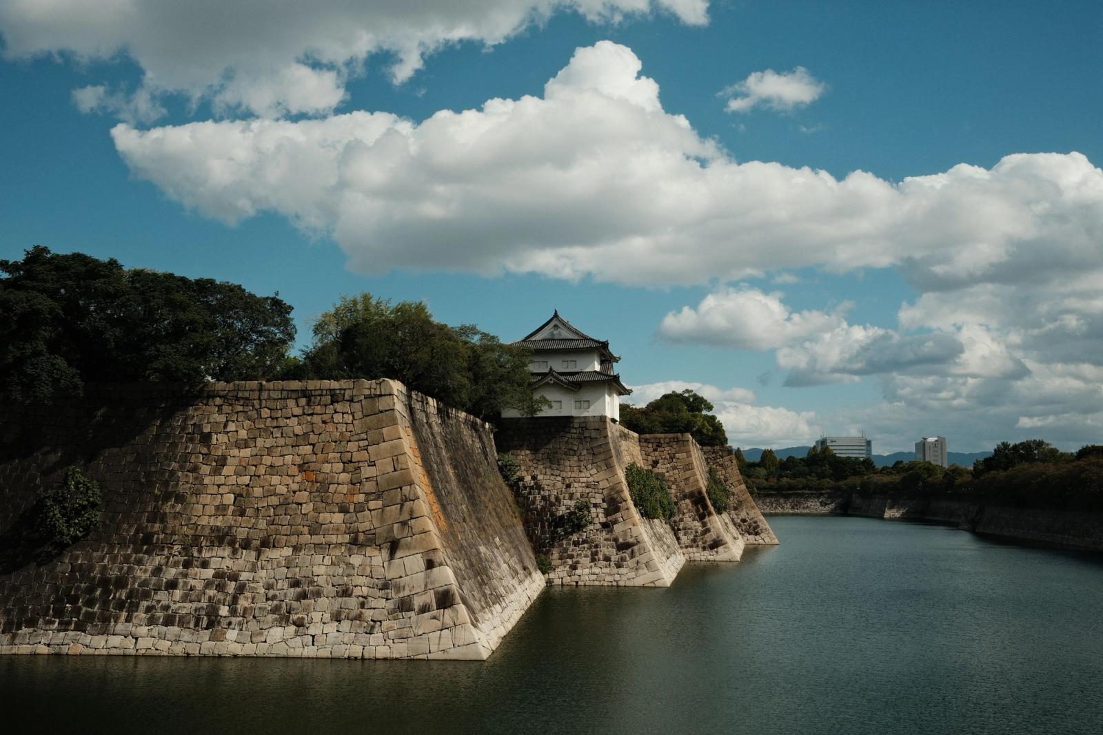 A scenic view of Osaka Castle's moat and walls under a bright blue sky with clouds in Osaka, Japan