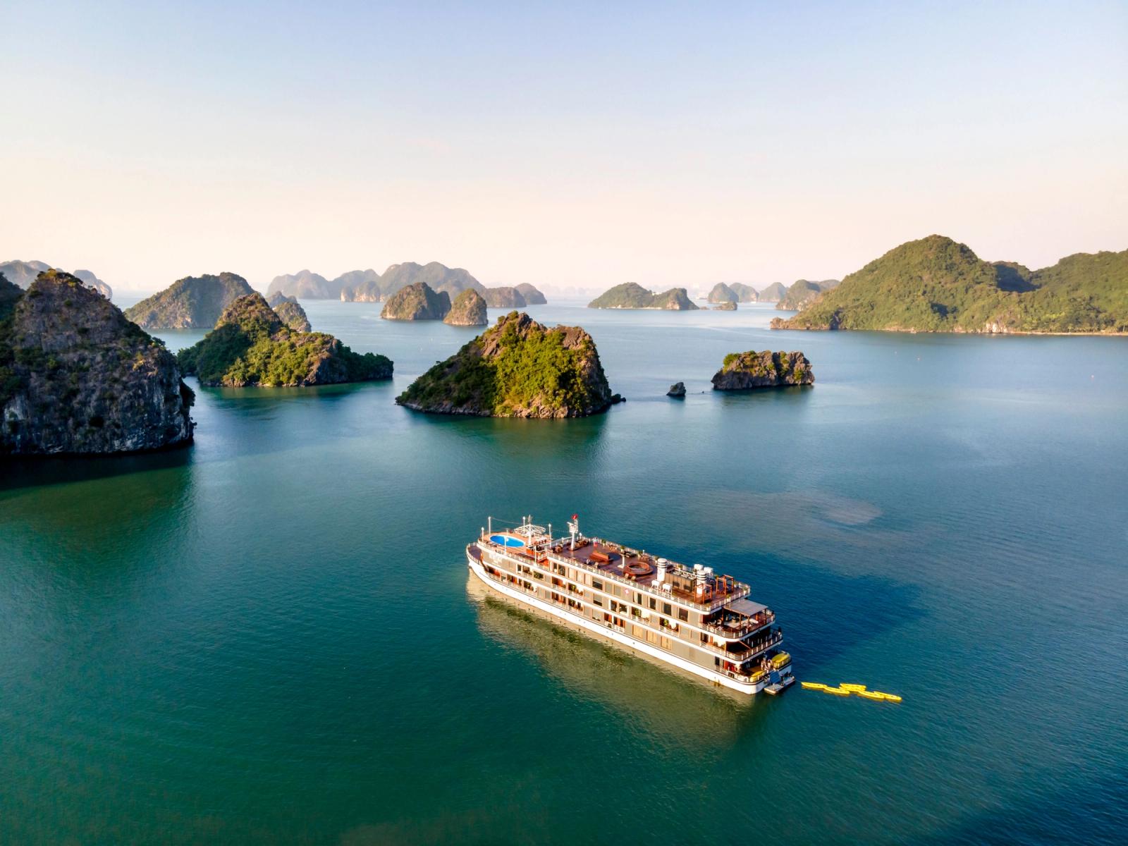 Aerial view of a cruise ship navigating through Halong Bay, featuring scenic limestone islands and calm waters