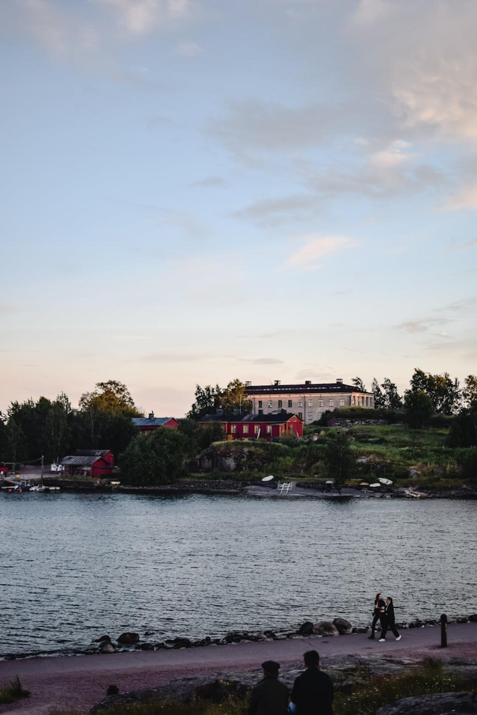 Waterfront building glowing at dusk with figures strolling the shore path
