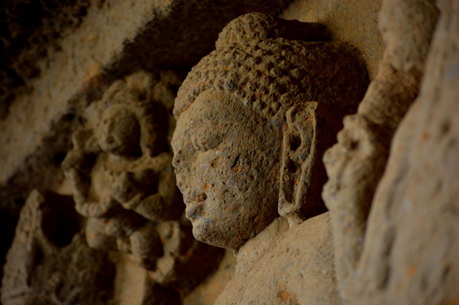 Weathered stone carving of a serene figure among rock-cut relief panels