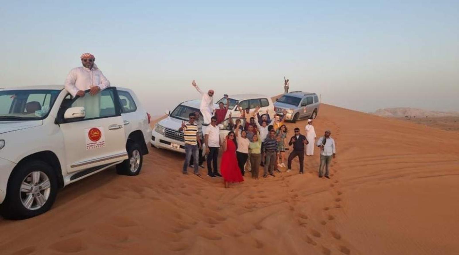 A group of people stands in the desert beside their vehicles 