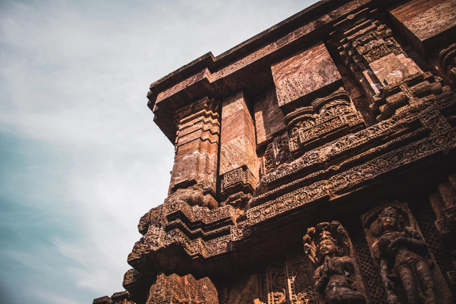 From below of ornamental carvings and sculptures of stone wall of ancient Konark Sun Temple located in India against cloudy sky