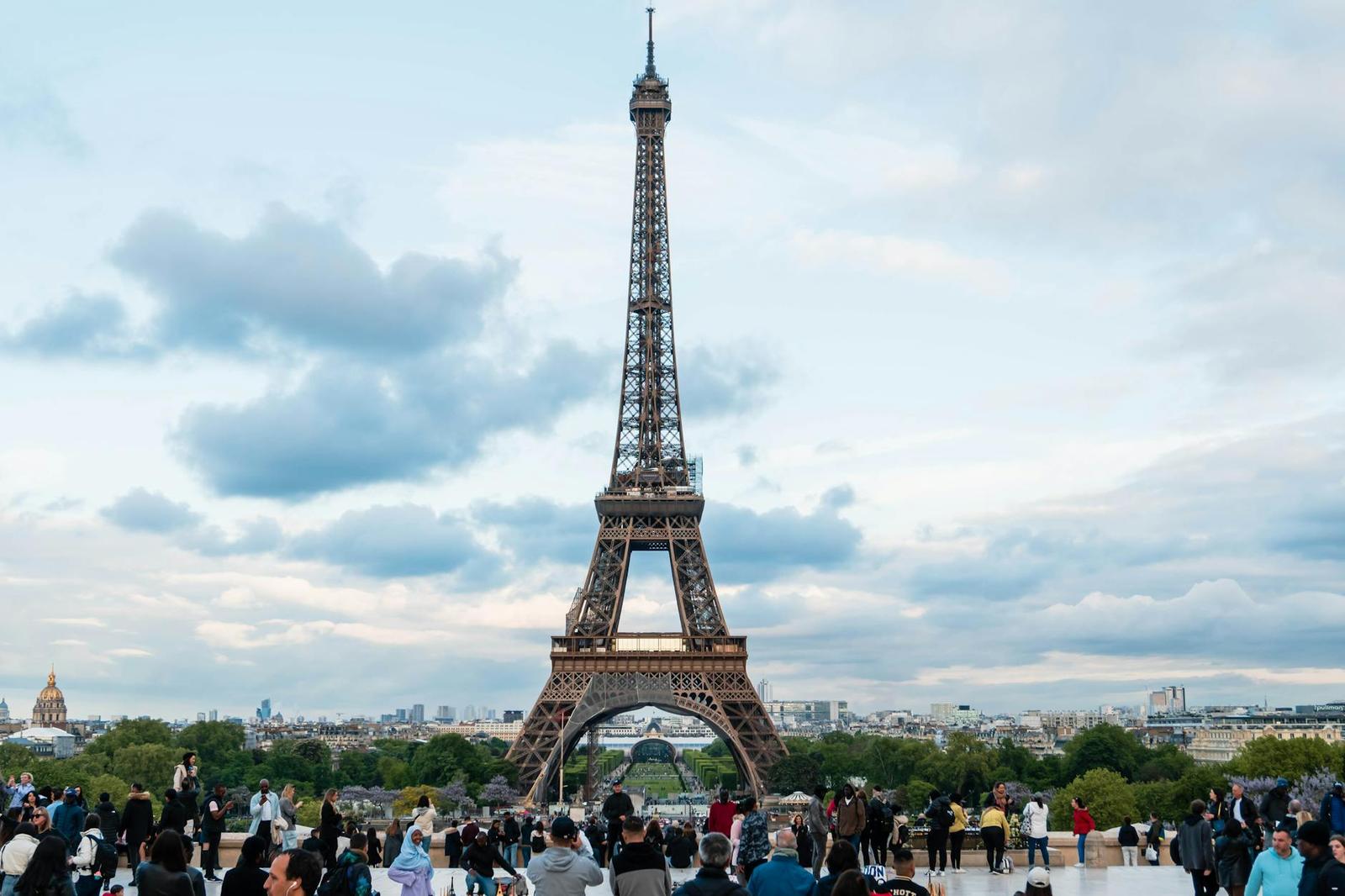 Iconic view of the Eiffel Tower in Paris surrounded by tourists on a cloudy day
