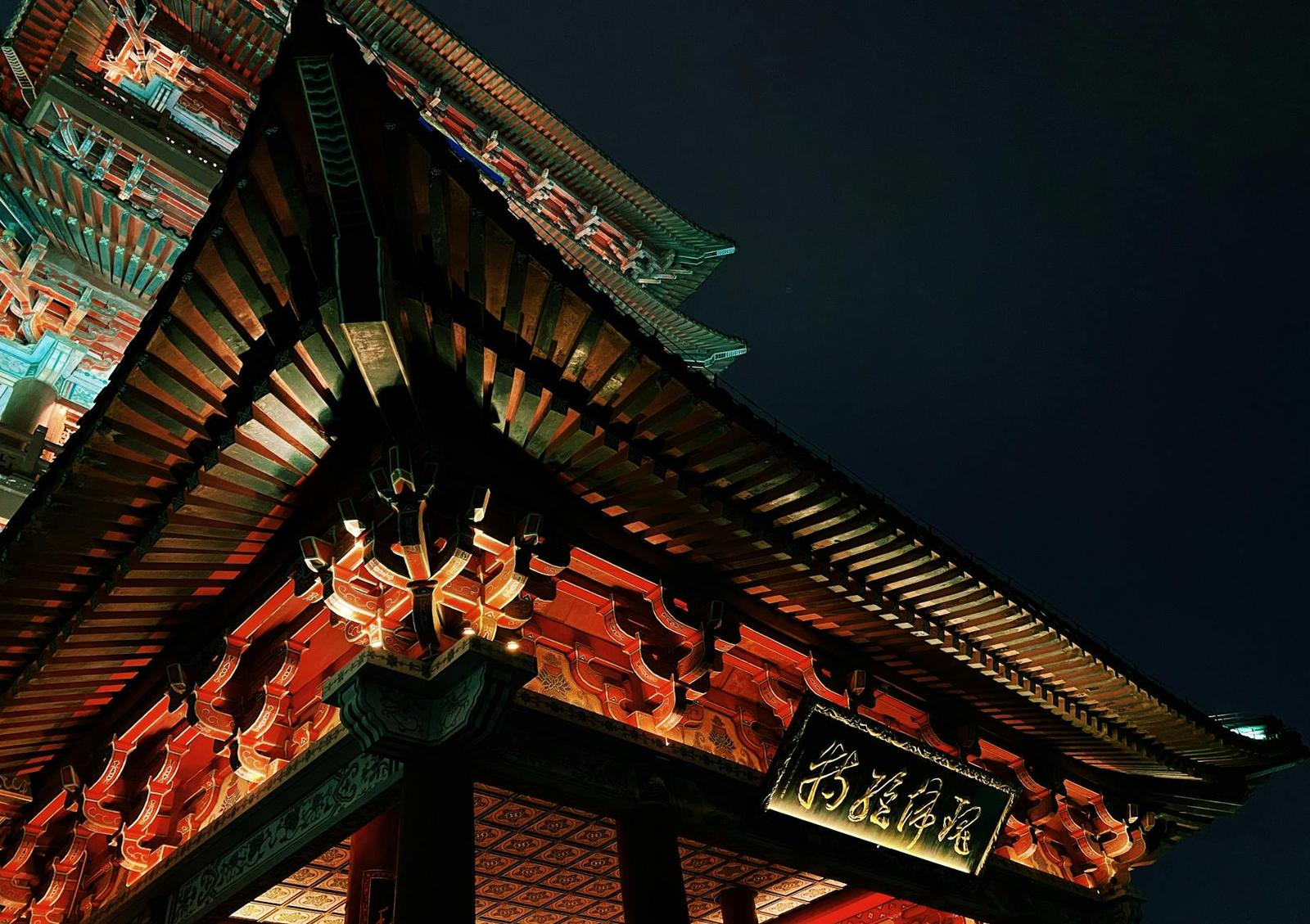 The illuminated corner of a temple roof with red and gold carved eaves at night