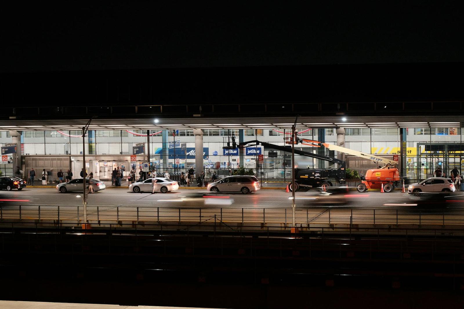 Motion-blurred traffic streaming past a brightly lit station building at night