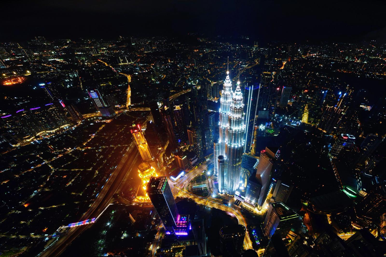 Aerial view of Kuala Lumpur cityscape at night, featuring the illuminated Petronas Twin Towers