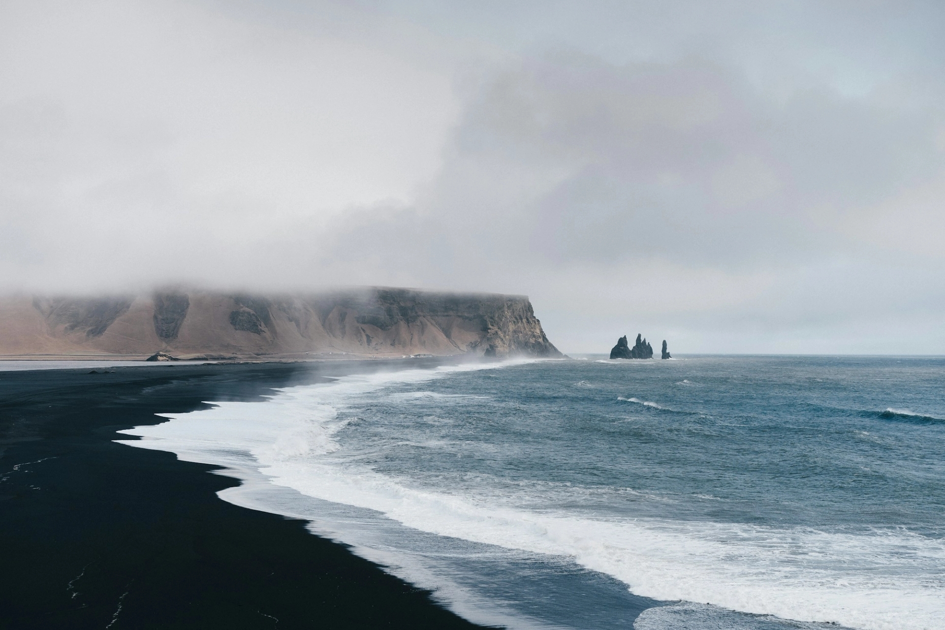 A black sand beach with sea stacks rising from misty waves