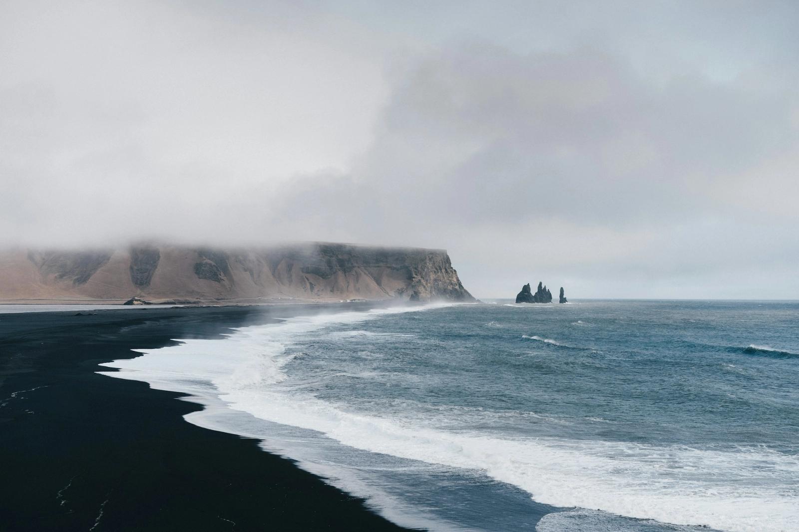 A black sand beach with sea stacks rising from misty waves