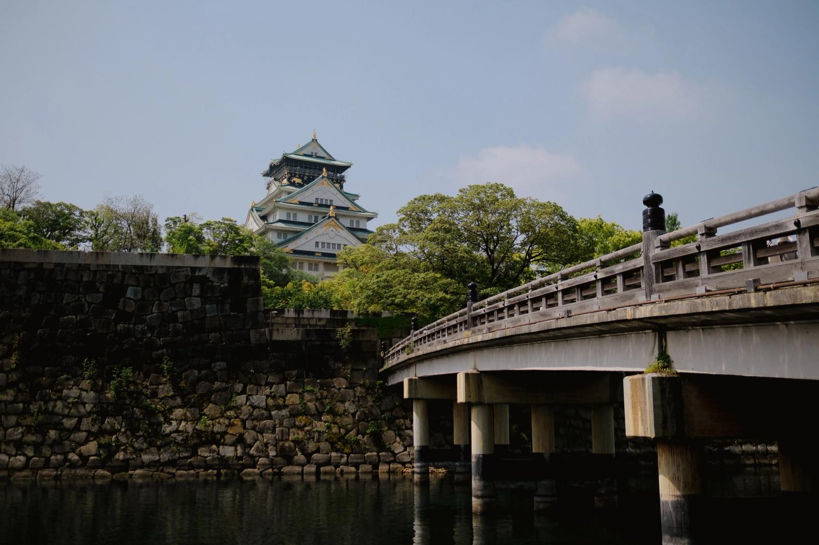 A picturesque view of Osaka Castle and nearby bridge surrounded by lush greenery