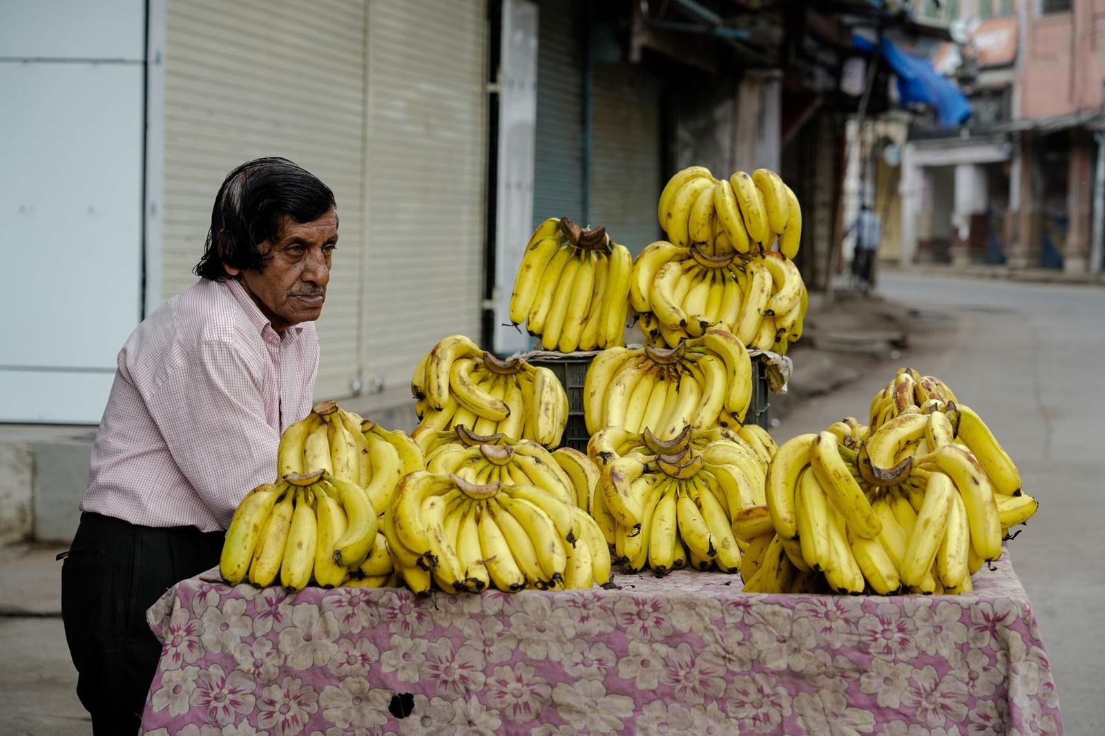 A street vendor stands beside a cart stacked with banana bunches