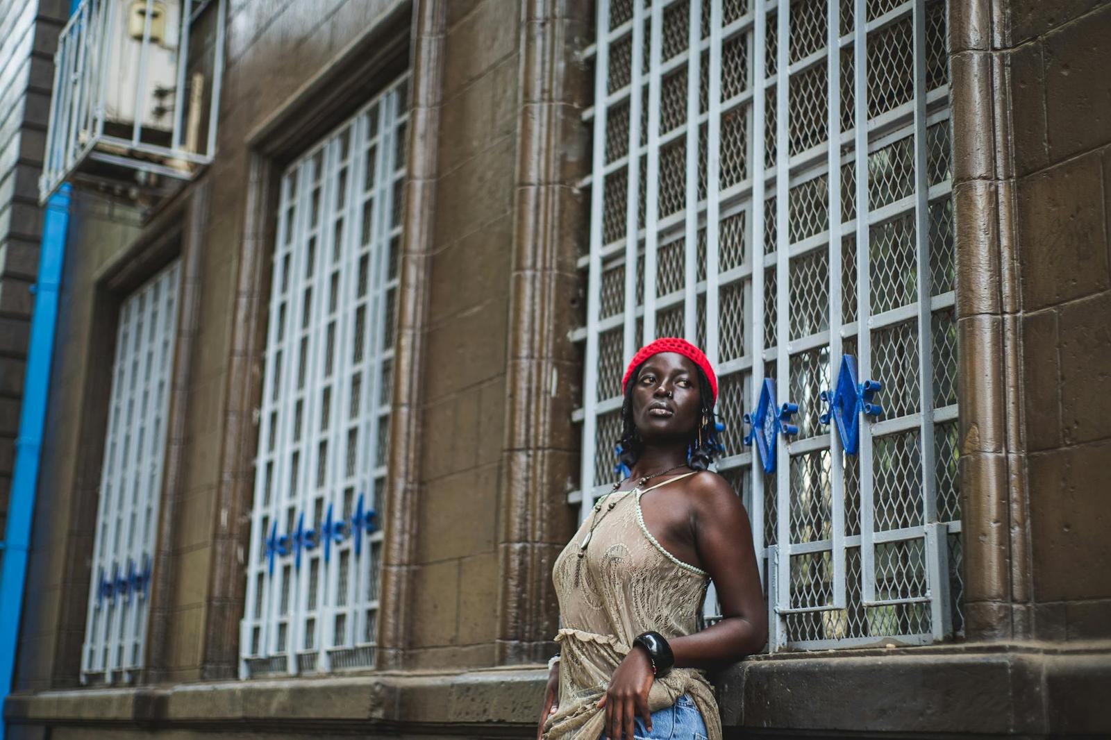 A woman in a red beret leaning against a barred window on a city street