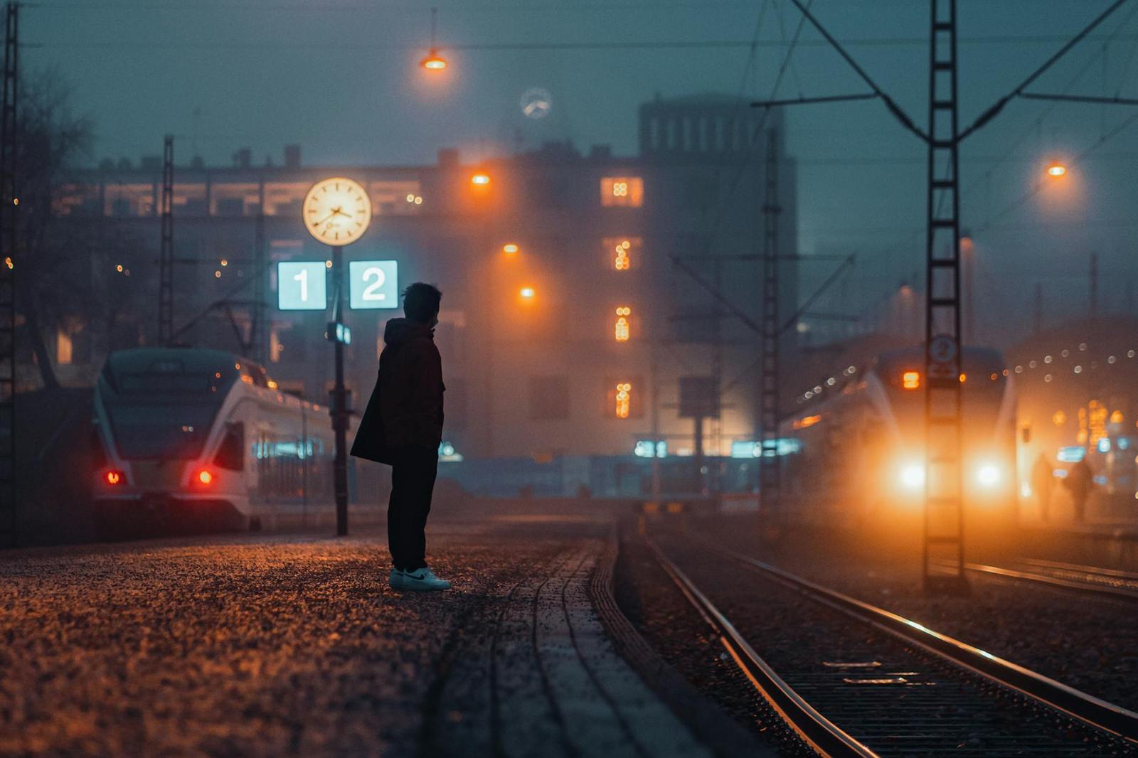 A figure standing alone on a foggy train platform at night