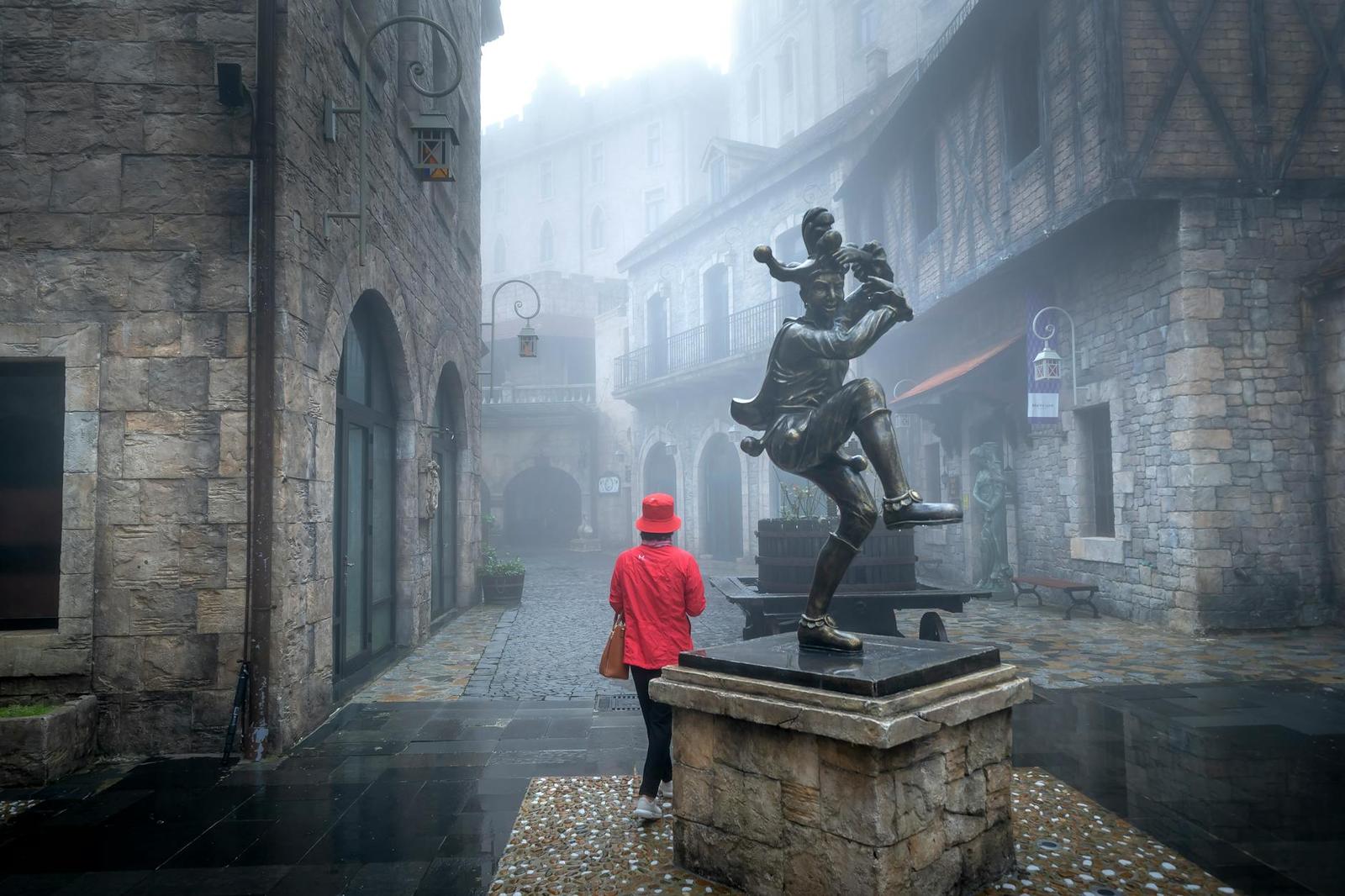 Person in a red coat approaching a bronze statue in misty fog