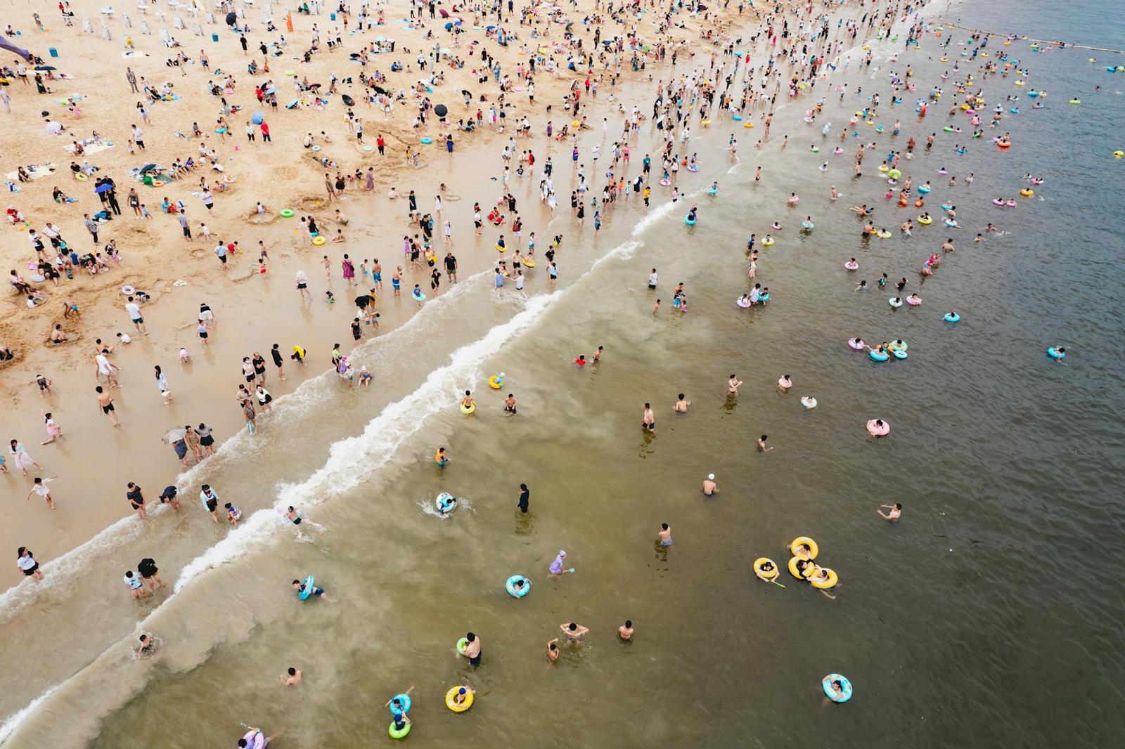Aerial view of a crowded beach with swimmers and colourful inflatable rings