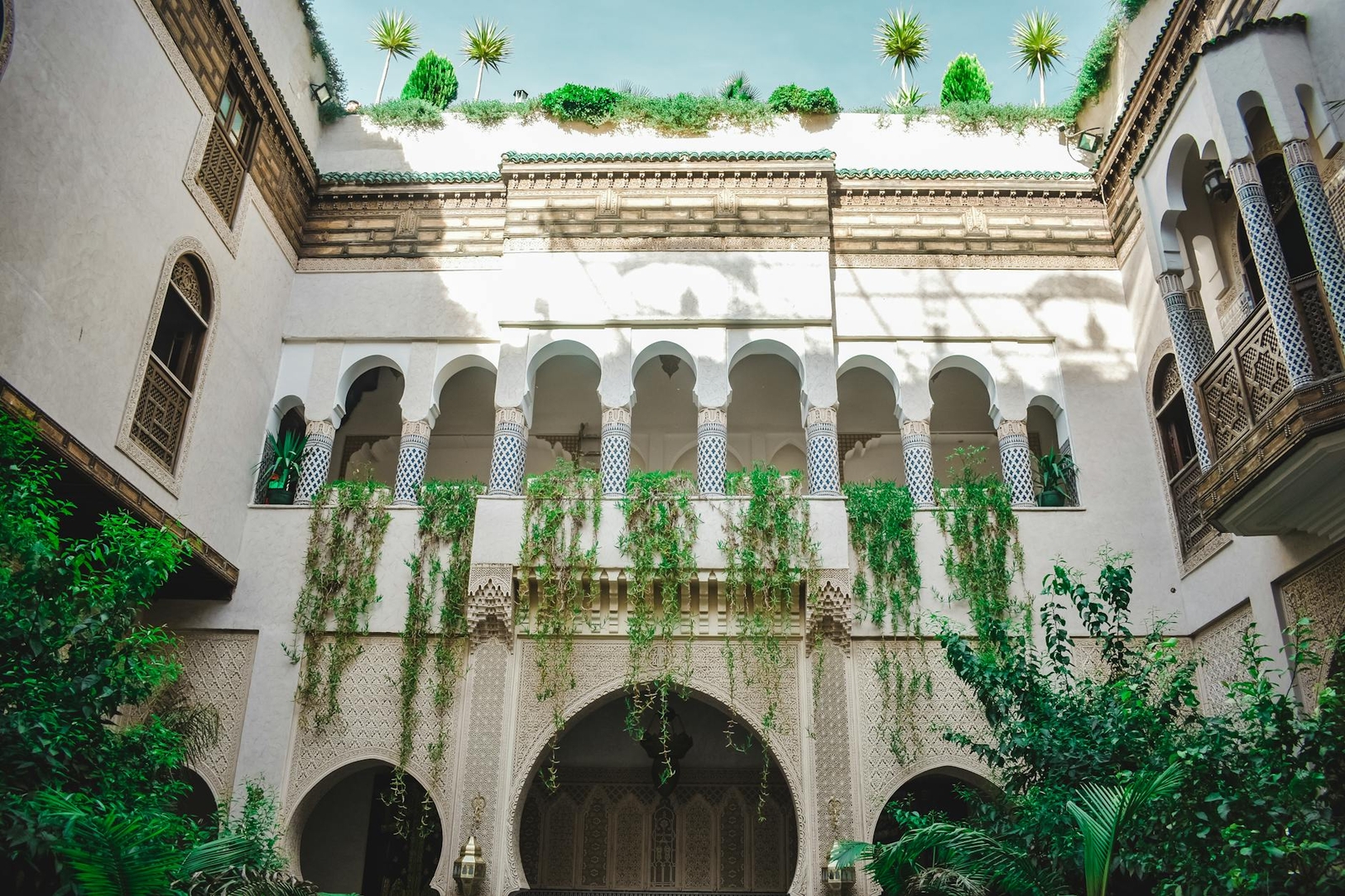 An arched courtyard facade draped in greenery below a rooftop garden