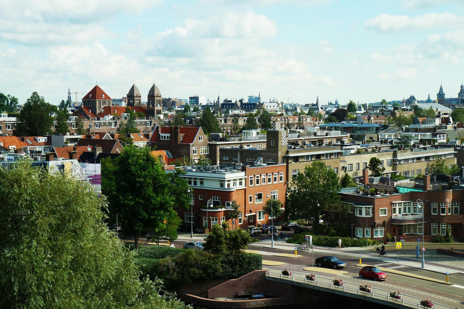 A city skyline of gabled rooftops and spires seen from an elevated bridge