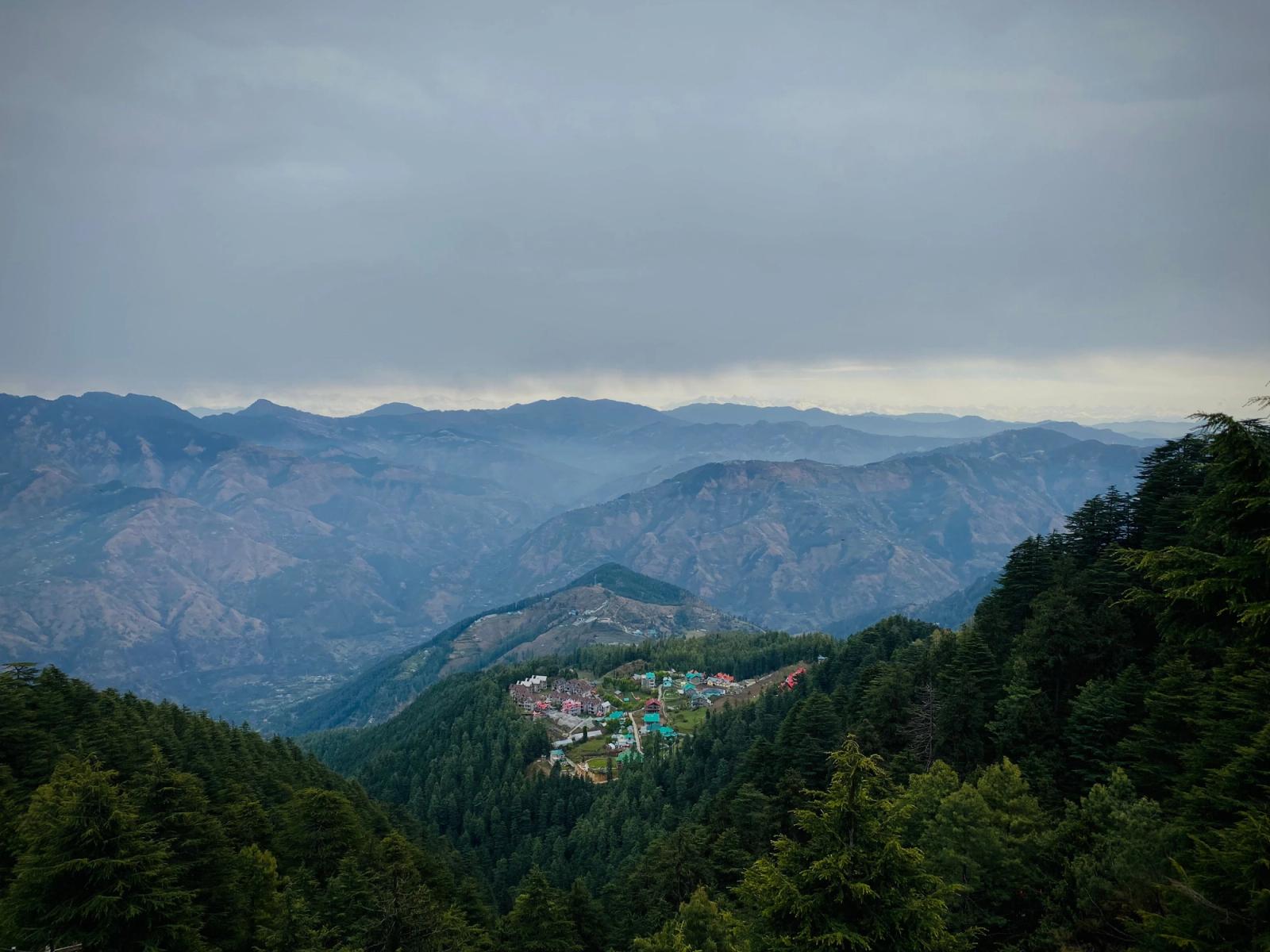 A serene view of a village nestled in the evergreen Shimla hills under overcast skies