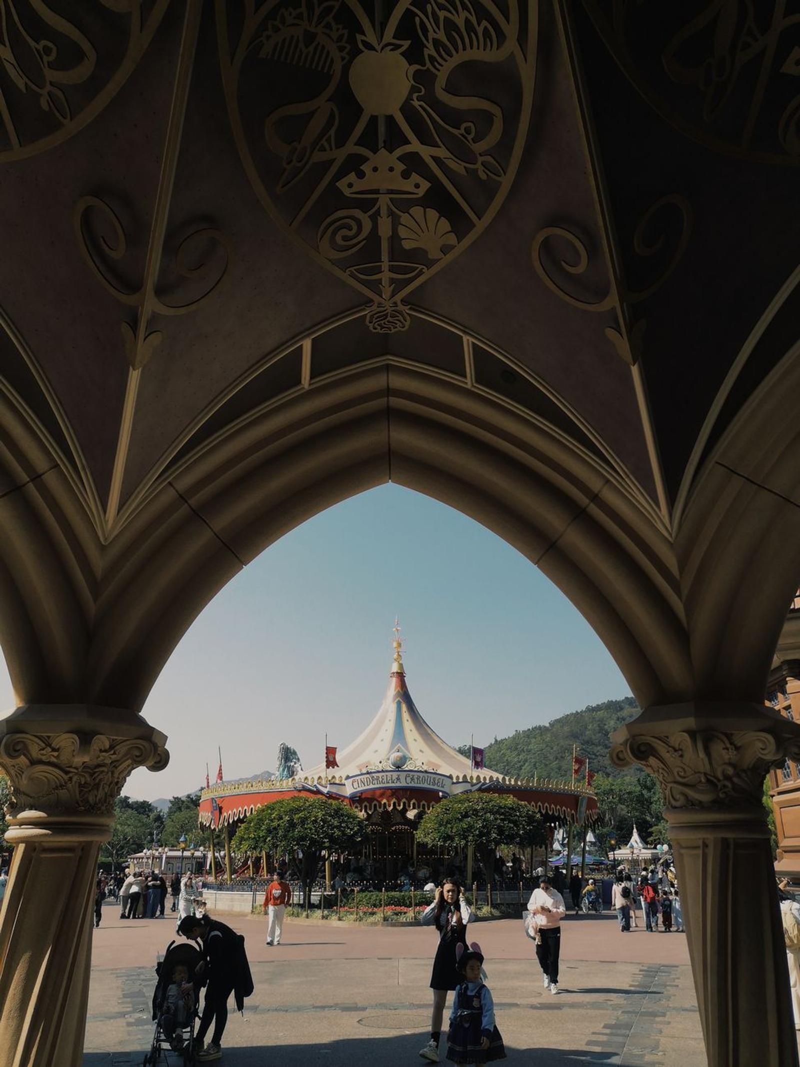 Stone archway framing a striped circus-tent pavilion and strolling visitors
