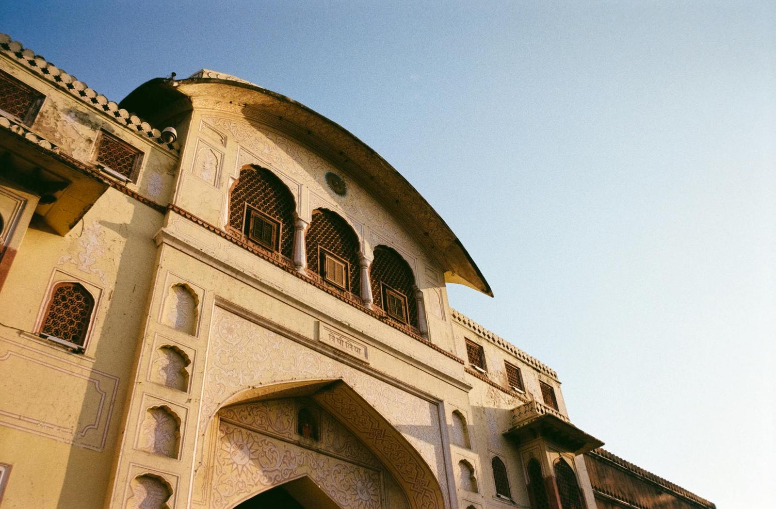 An arched sandstone gateway with carved balconies at sunset