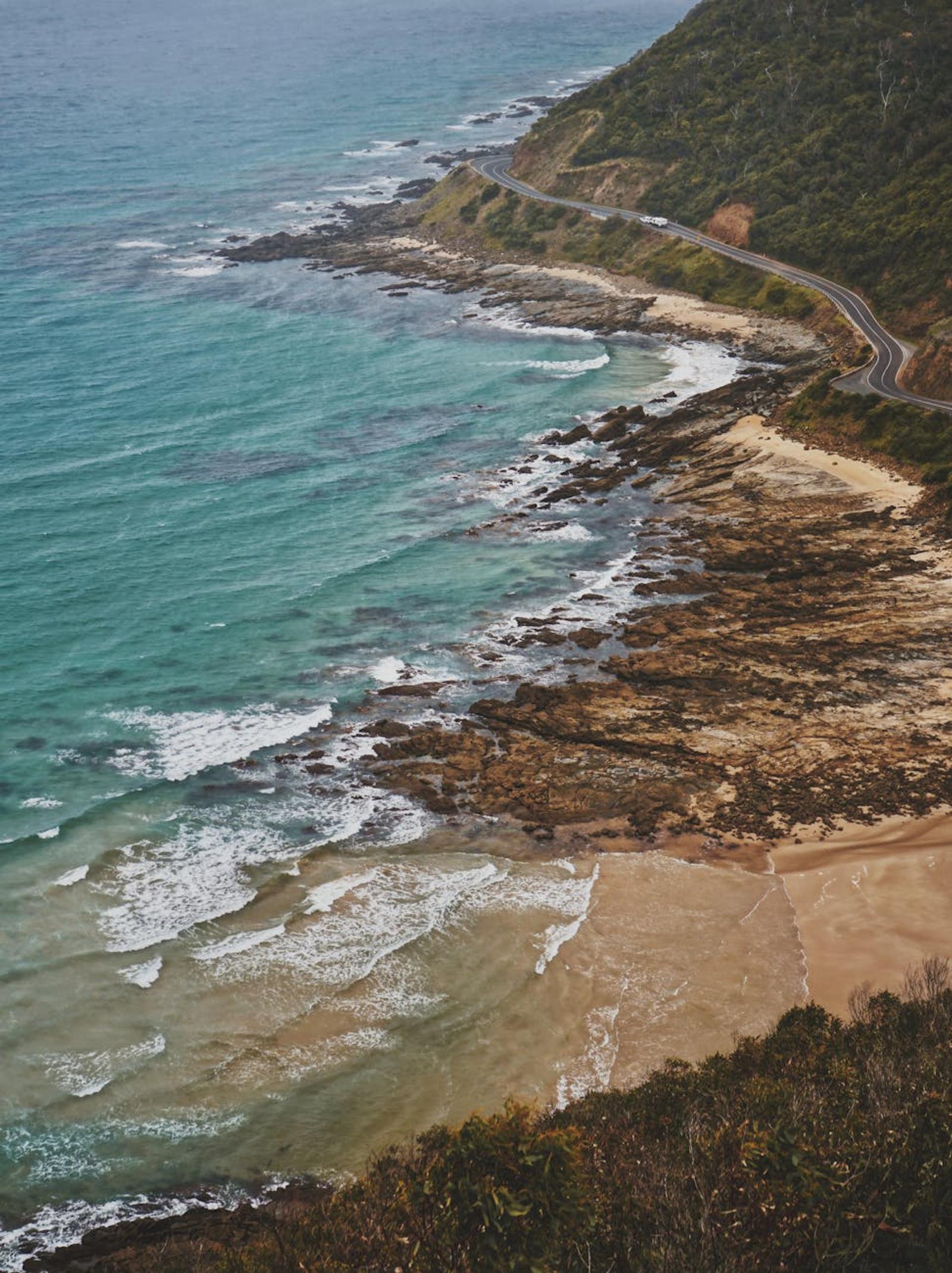 Stunning aerial view of a curving road along a rocky seaside landscape with waves crashing on the shore